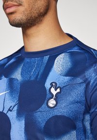 Blauwe sportieve jersey met cirkelpatronen, voorzien van een geborduurd logo op de linkerkant van de borst en een ronde halslijn. Gemaakt van lichtgewicht stof.