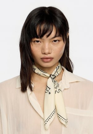 Kreemist siidist sall mustade abstraktsete mustritega, seotud kaela ümber väikese metallist südame aksessuaariga. Kandi peal heledat pluusi.