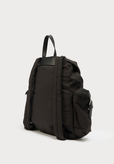 Μαύρο μαξιλαρωμένο σακίδιο με επάνω χειρολαβή, δύο πλαϊνές τσέπες και δερμάτινες λεπτομέρειες. Διαθέτει λεία υφή και κλείσιμο με φερμουάρ.