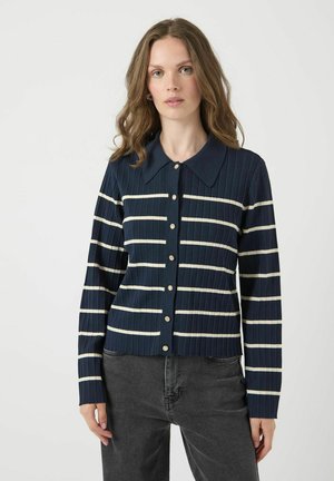 Námořnický žebrovaný cardigan s vodorovnými krémovými pruhy, límečkem a velkými knoflíky. Design zahrnuje dlouhé rukávy a přiléhavý siluetu.