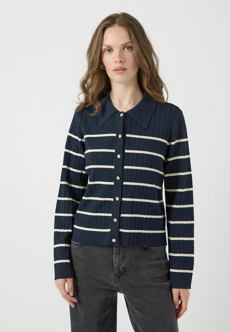 Marinblå ribbad cardigan med horisontella krämfärgade ränder, en krage och stora knappar. Designen har långärmar och en figursydd silhuett.