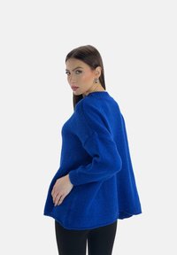 Maglione lavorato a maglia oversize di un blu royal con una finitura testurizzata, maniche lunghe e orlo curvo. Abbinato a leggings neri.