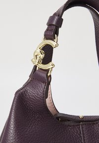 Borsa a tracolla in pelle viola con superficie texturizzata, dotata di una chiusura dorata e dettagli sulla tracolla. Forma leggermente strutturata con cuciture evidenti.
