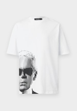 T-shirt en coton blanc avec un graphique linéaire noir d'un visage sur le devant. Manches courtes et col rond. Design simple.