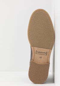 Sole di scarpa in suede grigio con fondo in gomma testurizzata; presenta l'etichetta "FATTO A MANO" e la taglia 41 su una superficie color beige chiaro.