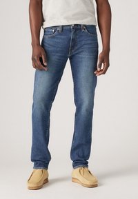 Blå denimjeans med rakt ben. Har en klassisk femfickdesign och subtila slitningar. Matchas med ljusfärgade mockasiner.