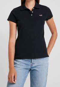 Svart polo t-shirt i bomull, med krage, korta ärmar, treknapplås och en liten logotyp på bröstet.