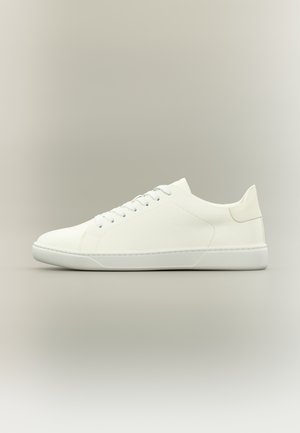 Balts zemās virsmas sporta apavu pāris ar šņorēm, gludu ādas virsmu un platu gumijas zolīti uz neitrāla fona.