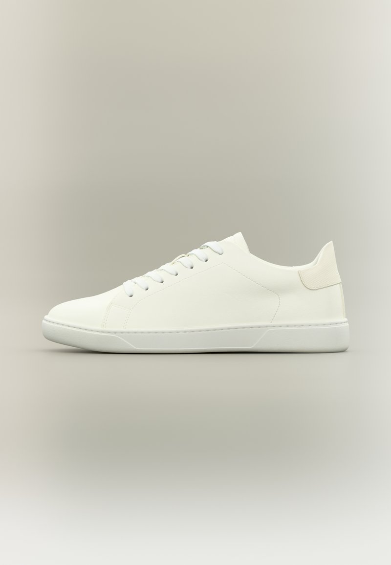 Baskets basses blanches avec lacets, tige en cuir lisse et semelle plate en caoutchouc sur un fond neutre.