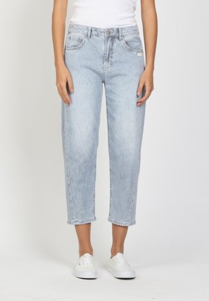 Person wearing light blue cropped jeans and white sneakers, standing against a plain white background.