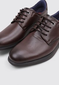 Zapatos de cuero marrón con un acabado suave, que cuentan con una puntera redondeada, seis ojales y cordones oscuros. El interior está forrado en azul.