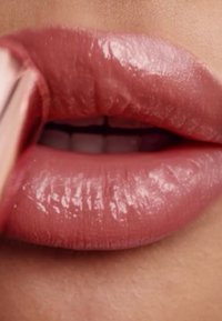 Lipstick aanbrengen op volle, glanzende roze lippen. De lippen hebben een gladde textuur en een natuurlijke, zachte roze tint, met een opvallende glans.