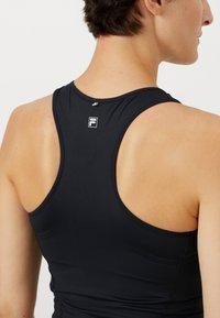 Čierny športový top s dizajnom na chrbte typu racerback, ktorý má malé logo na zátylku, vyrobený z hladkej a elastickej tkaniny.