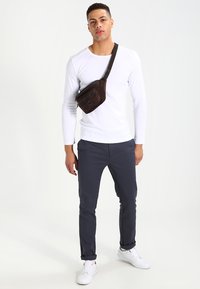 White long-sleeve shirt, dark grey pants, and a brown crossbody bag. The bag features a zip pocket; white sneakers complete the look.
