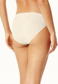 Mutande hipster in cotone beige con superficie liscia, elastico in vita e senza cuciture visibili, viste da dietro.