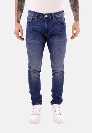 Jeans skinny in denim blu medio con leggeri effetti di sbiadimento, design a cinque tasche e zip a bottone. Abbinati a sneakers bianche.