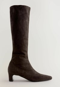 Bota de ante marrón hasta la rodilla con punta afilada y un tacón bajo y resistente. Textura suave con detalles de costura sutil.