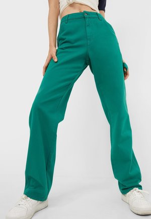 Groene wijde broek van katoen, met een hoge taille, zichtbare stiksels en een knoopsluiting aan de voorkant. Gepaard met witte sneakers.