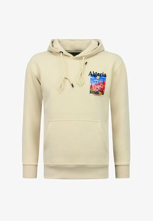 Beige hoodie met voorzak, capuchon met trekkoord en een kleurrijke Algerije-patch op de borst, met een stadsgezicht, blauwe lucht en zon.