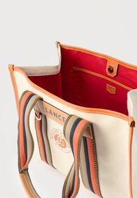 Υφασμάτινη τσάντα tote με πορτοκαλί λεπτομέρειες, μπλε και πορτοκαλί ριγωτές λαβές, κόκκινη επένδυση στο εσωτερικό, λογότυπο μπροστά και κλείσιμο με κουμπί.