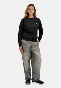 Black sweatshirt with round neckline and ribbed cuffs, paired with gray baggy jeans and black sneakers with white soles.