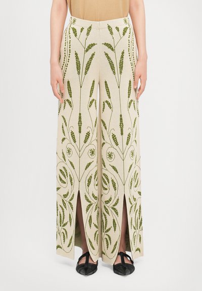 Pantaloni beige a gamba larga con intricati ricami floreali verdi e spacchi laterali, realizzati in un tessuto testurizzato con una finitura liscia.