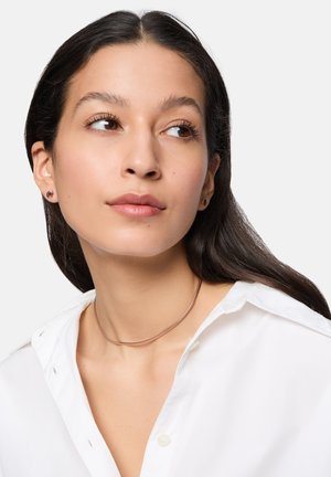 Collana choker con un design metallico sottile e liscio in argento. Il modello indossa una camicia bianca con bottoni, mettendo in mostra i gioielli eleganti.
