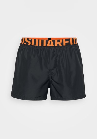 Schwarze Bade Shorts für Männer mit einem orangefarbenen elastischen Bund, versehen mit fettem schwarzen Text, auf einem weißen Hintergrund präsentiert.
