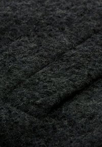 Tissu noir texturé avec des fibres grises subtiles. La surface est duveteuse, mettant en valeur un motif tissé dense. Contient des touffes douces et enroulées.