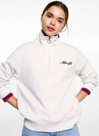 Lichtgrijze hoodie met rits en hoge kraag, voorzien van een klein geborduurd logo en contrasterende rode en paarse accenten op de manchetten.