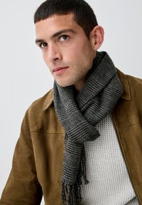 Écharpe à motif gris en tissu doux, portée autour du cou. Présente des bords frangés et un mélange de tons gris clair et foncé.