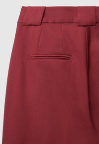 Bordeauxfarbene Hosen mit glatter Textur, weitem Bund und einer einzelnen Gesäßtasche mit subtiler Nahtdetails.