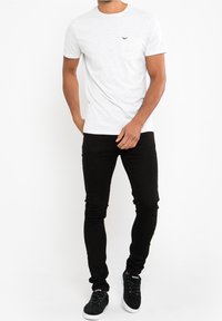 Bílé tričko s krátkými rukávy, kulatým výstřihem a náprsní kapsou. Kombinováno s černými úzkými džíny a černými teniskami s bílou podrážkou.