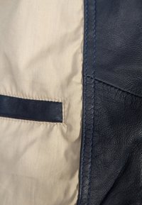 Sisäosa laivastonsinistä nahkaa ja ruskeaa kangasta, jossa on laivastonsininen koristeriipputasku, näkyvät ompeleet ja sileä pinta.