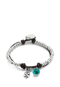 Pulsera de cuentas de plata con un cordón de cuero marrón, que presenta un pequeño charm de vidrio color teal y un colgante de trébol de plata. Cierre ajustable.
