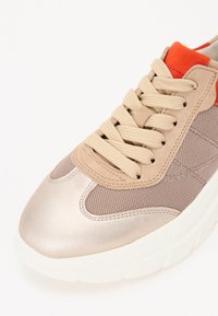 Beżowy sneaker z metalicznymi złotymi akcentami, teksturowanymi panelami mesh i beżowymi sznurowadłami. Posiada białą podeszwę i pomarańczowe detale przy kołnierzu.