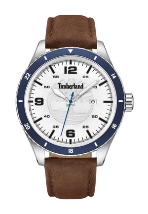 Reloj Timberland con caja plateada, esfera blanca, bisel azul marino, correa de cuero marrón y acento azul en la manecilla de los segundos. Marcadores de hora negros.