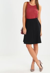 Svart kjol med insetter, tillsammans med en röd linne. Tillbehören inkluderar en brun axelväska; grå mocka klackar fulländar outfiten.