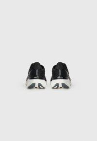 Zapatillas deportivas negras con una parte superior texturizada, mediasolados blancos y una suela de goma gris. Presentan detalles del logo en el talón y un diseño aerodinámico.