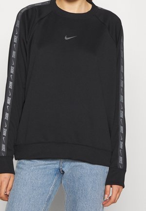 Czarna bluza Nike z długim rękawem, logo na piersi oraz firmowymi paskami na rękawach, noszona z jasnoniebieskimi dżinsami.