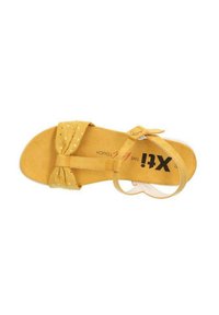 Sandal in camoscio giallo con un dettaglio a fiocco sulla cinghia delle dita, suola piatta e cinghia alla caviglia. Presenta piccoli pois dorati sul fiocco.
