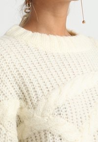 Chunky krämfärgad stickad tröja med en ribbad krage, prydd med ett kabelmönster. Den strukturerade, fluffiga garnet ger värme och visuell intress.