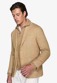Lysebrun blazer med en struktureret overflade, udstyret med en notch-krave, enkelt knaplukning og for-lygte lommer over en matchende sweater.