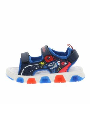 Sandalo per bambini blu e rosso con grafica di dinosauro, macchie di vernice, due cinturini in velcro e suola bianca con accentature blu e rosse sul battistrada.