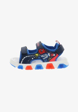Sandalo per bambini blu e rosso con grafica di dinosauro, macchie di vernice, due cinturini in velcro e suola bianca con accentature blu e rosse sul battistrada.