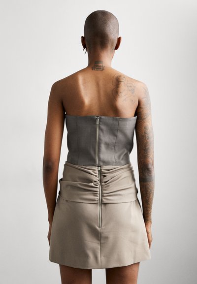 Strapless, gray top with a zipper at the back, paired with a beige, ruched mini skirt featuring a back zipper. Smooth texture and simple design.