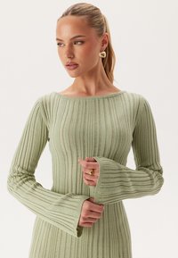 Robe tricotée côtelée vert clair avec de longues manches évasées et un large décolleté. Caractérisée par des rayures verticales et une finition douce et texturée.