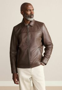 Barna bőrdzseki cipzárral, gallérral és két oldalzsebbel. Simaság jellemzi, fittebb fazonú, finom varrástechnikával.