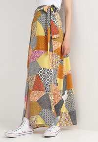 Lunga gonna in patchwork con vari modelli floreali e geometrici in giallo, nero, rosa e arancione. Vita con lacci, presenti fessure laterali.