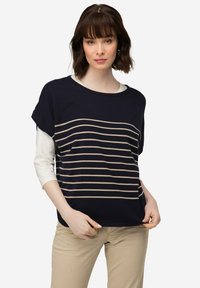 Námořnická modrá pletená halenka s béžovými vodorovnými pruhy, krátkými rukávy a širokým výstřihem. Nositá přes bílou košili s dlouhým rukávem. Volný střih.